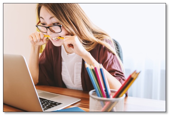 Picture of a woman looking intently at a laptop while biting on a pencil, communicating the effort needed for good dementia training. 